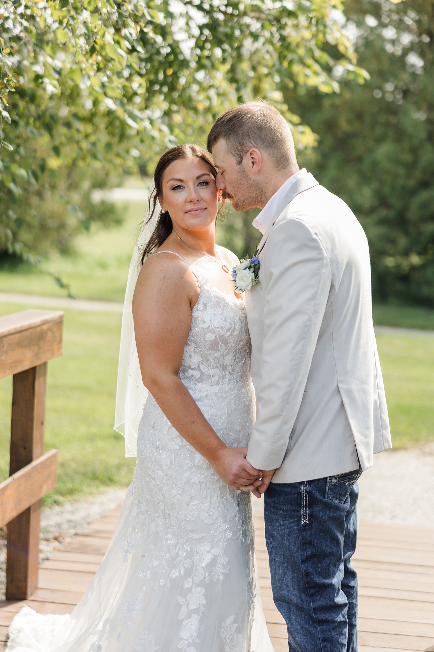 Ryan gently nuzzles Cassie as the breeze blows through her hair as they stand on a small wooden bridge at River Valley Orchards | CB Studio