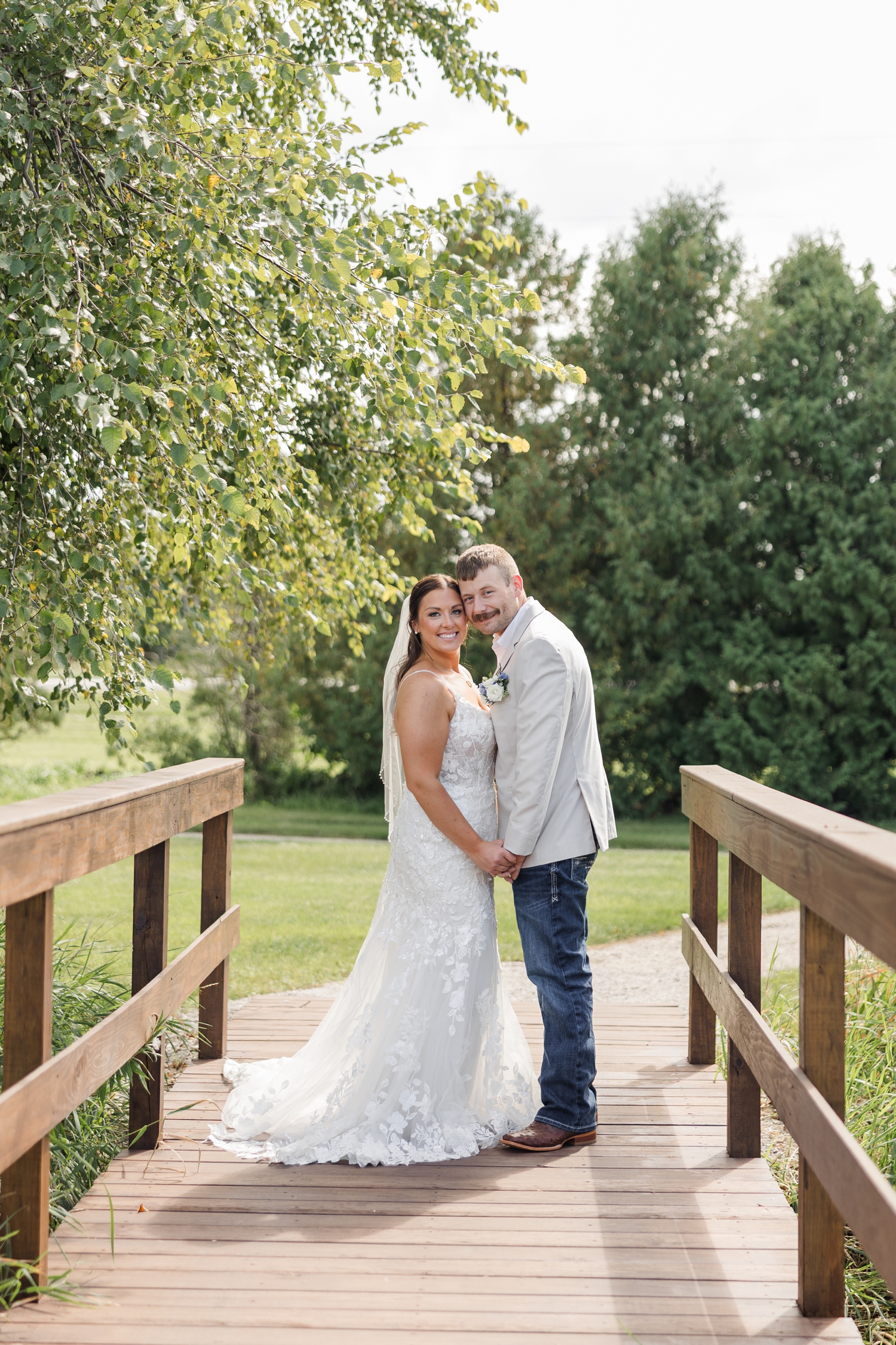 Ryan and Cassie stand belly button to belly button and hold hands as they stand on a small wooden bridge at River Valley Orchards | CB Studio