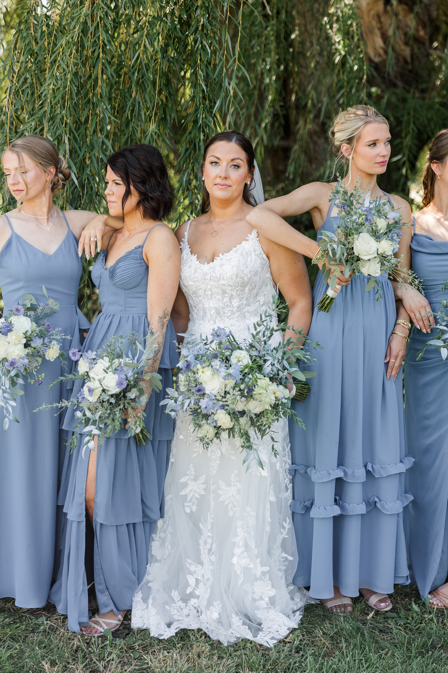 Cassie and her bridesmaids (dressed in blue) stand in a model pose while Cassie looks at the camera and the bridesmaids look off into the distance with a gorgeous weeping willow as the backdrop | CB Studio