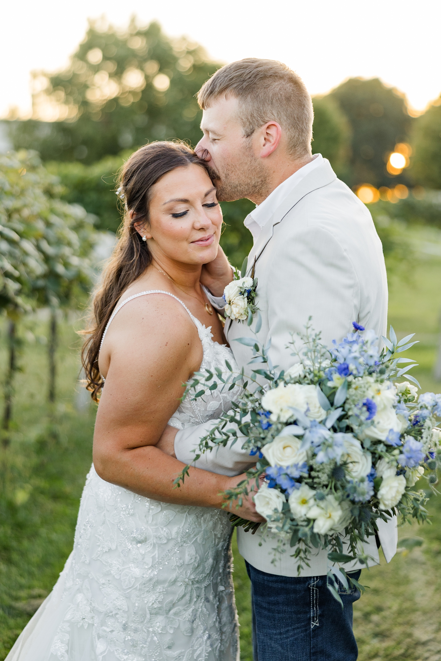 Ryan gently pulls Cassie in and kisses the top of her head amongst the vineyard of River Valley Orchards at sunset | CB Studio