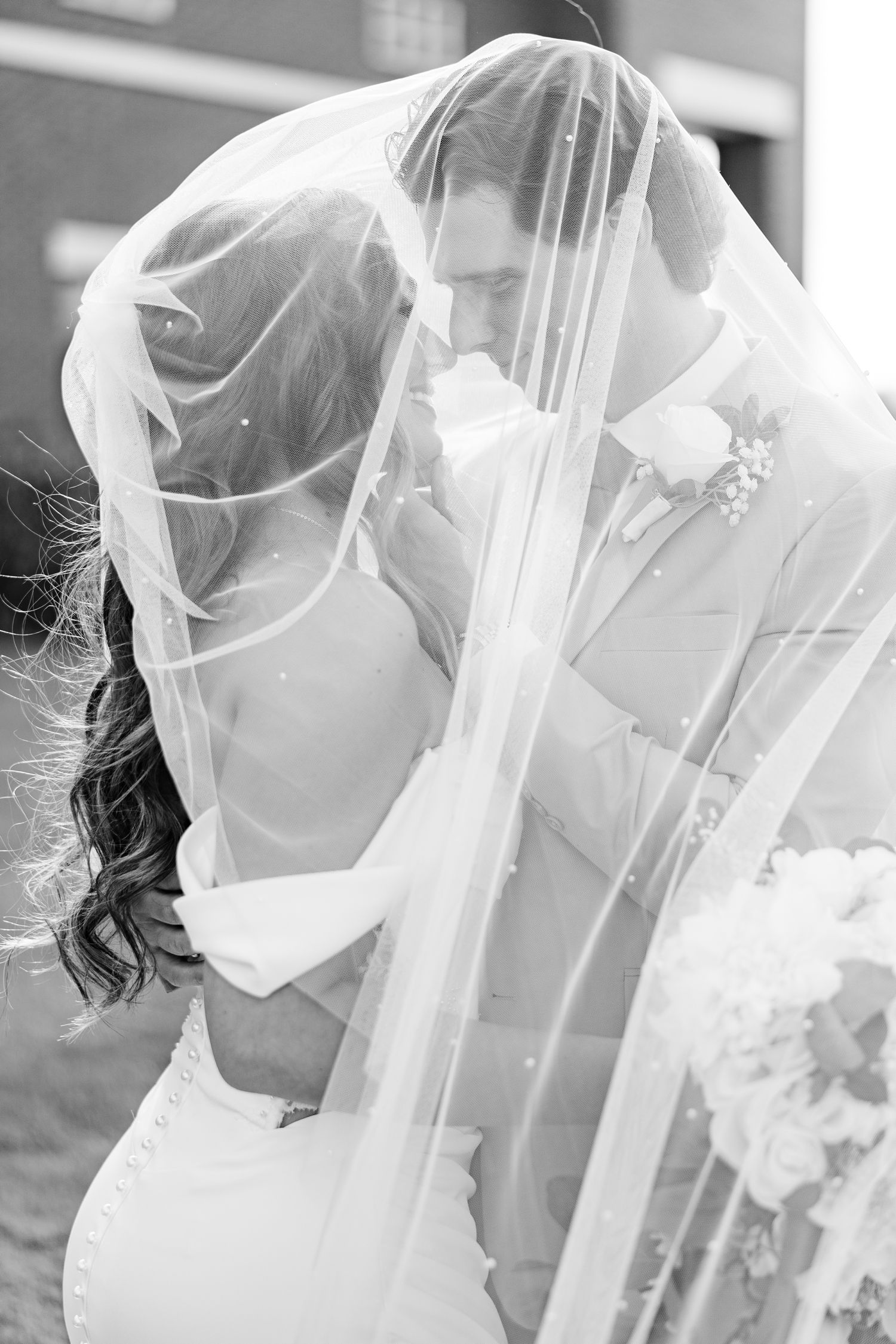 Bride and groom touches noses underneath the cathedral length veil adorned with pearls in front of the Holy Trinity Catholic Church in Fort Dodge, IA | CB Studio