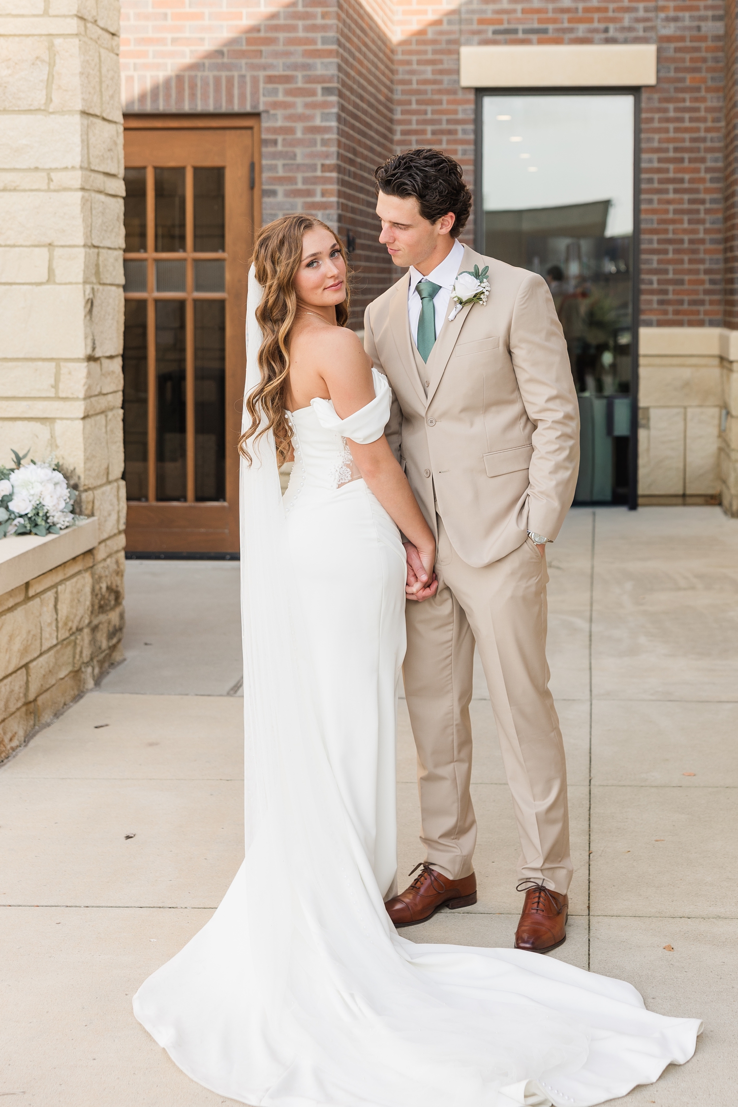 Groom looks intently at his bride as she looks at the camera in front of the Holy Trinity Catholic Church in Fort Dodge, IA | CB Studio