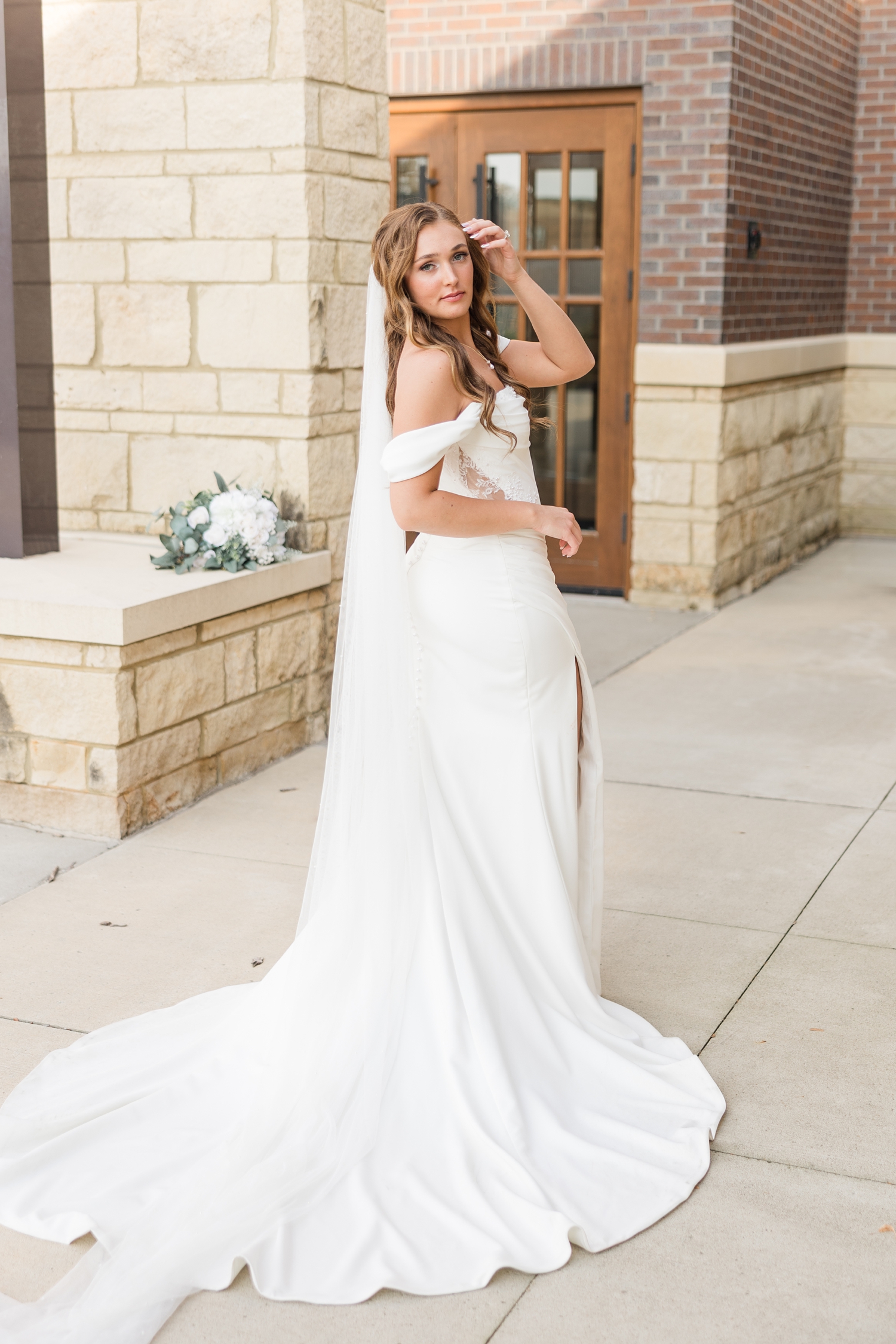 Bride model poses while brushing her hair out of her face in front of the Holy Trinity Catholic Church in Fort Dodge, IA | CB Studio