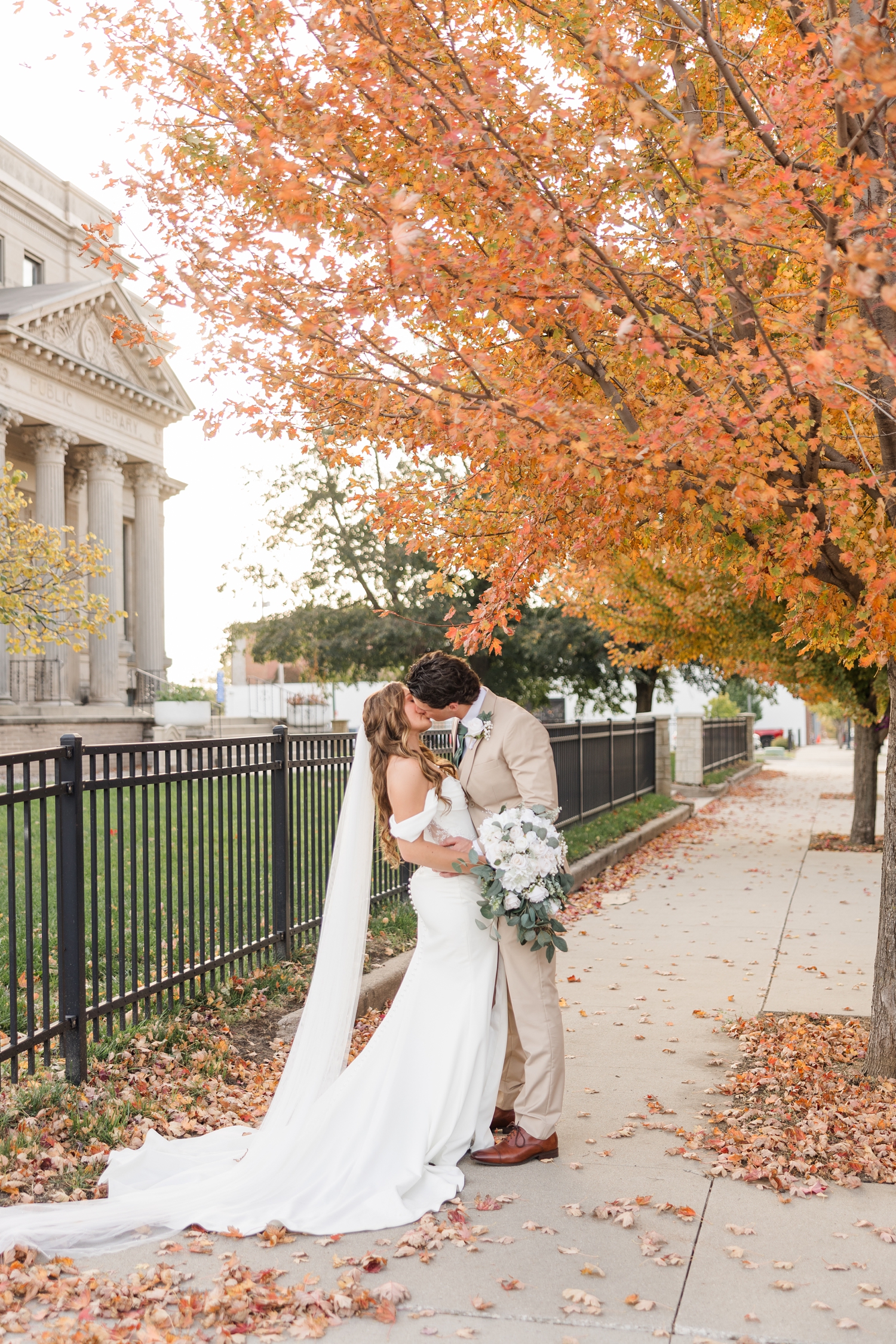 Bride and groom share a kiss under a peak fall maple tree on a sidewalk in downtown Fort Dodge, IA | CB Studio
