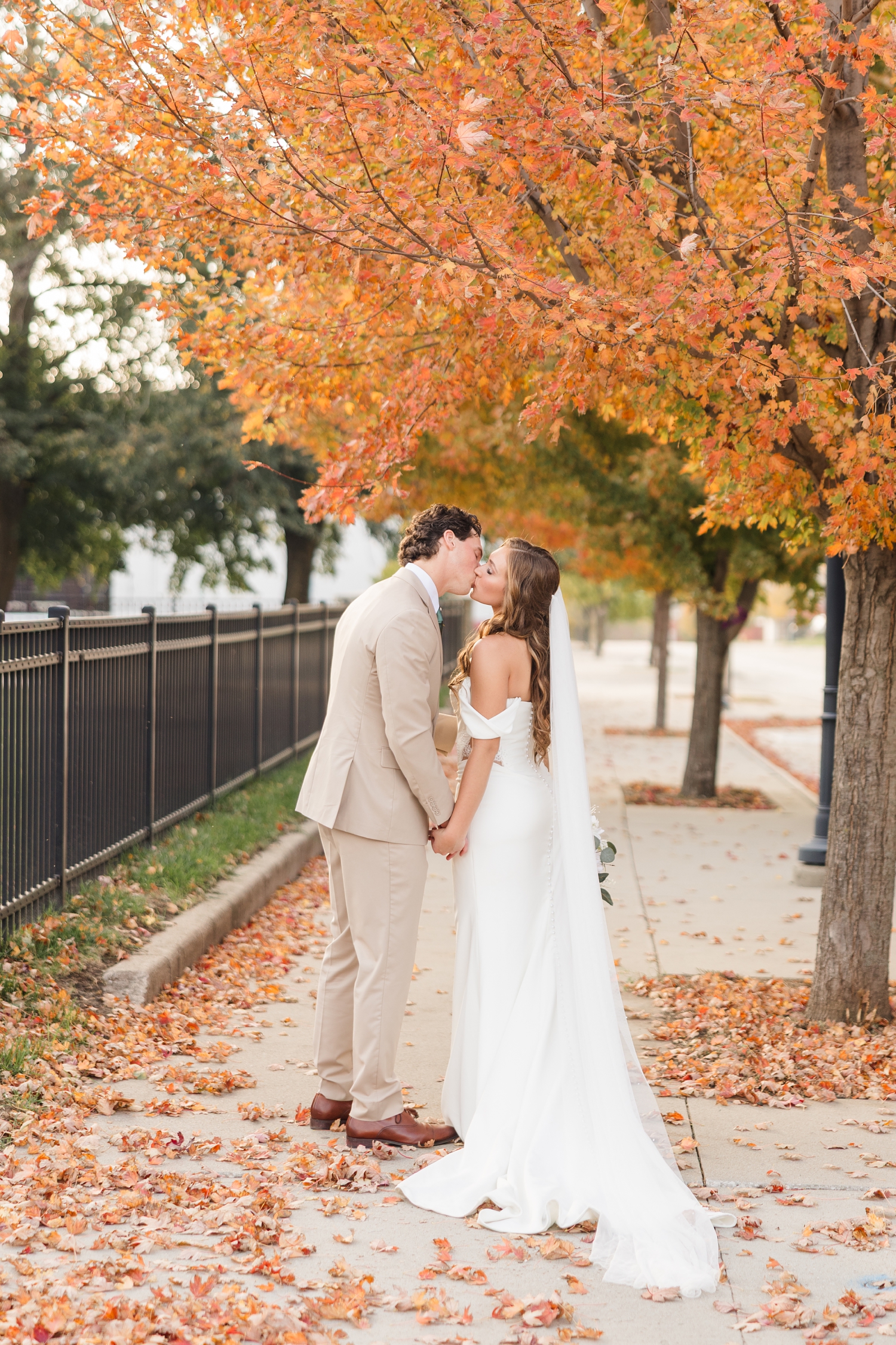 Bride and groom share a kiss under a peak fall maple tree on a sidewalk in downtown Fort Dodge, IA | CB Studio