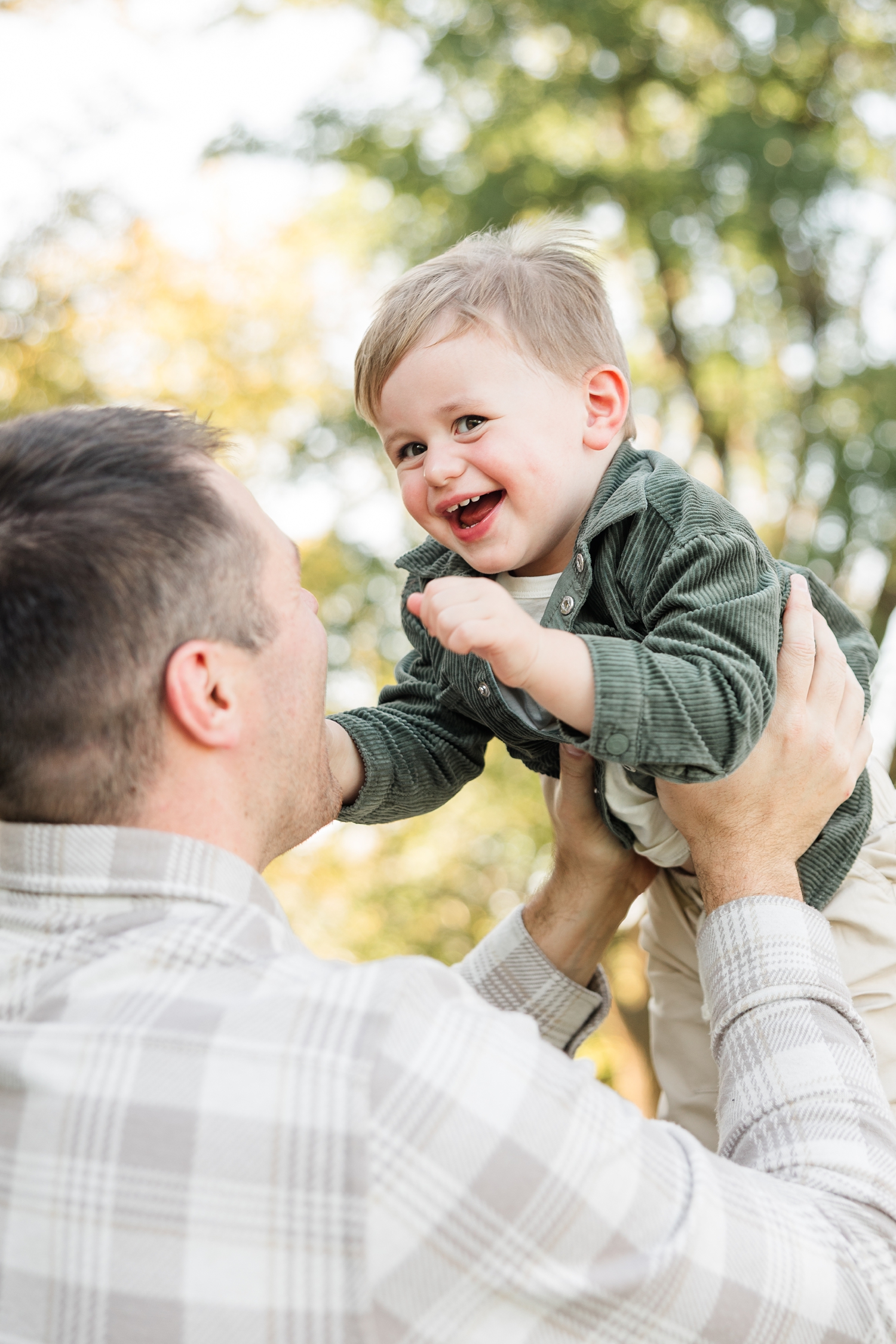 Cole throws his 2 year old son in the air as he is full of smiles and the fall leaves adorn the background | CB Studio