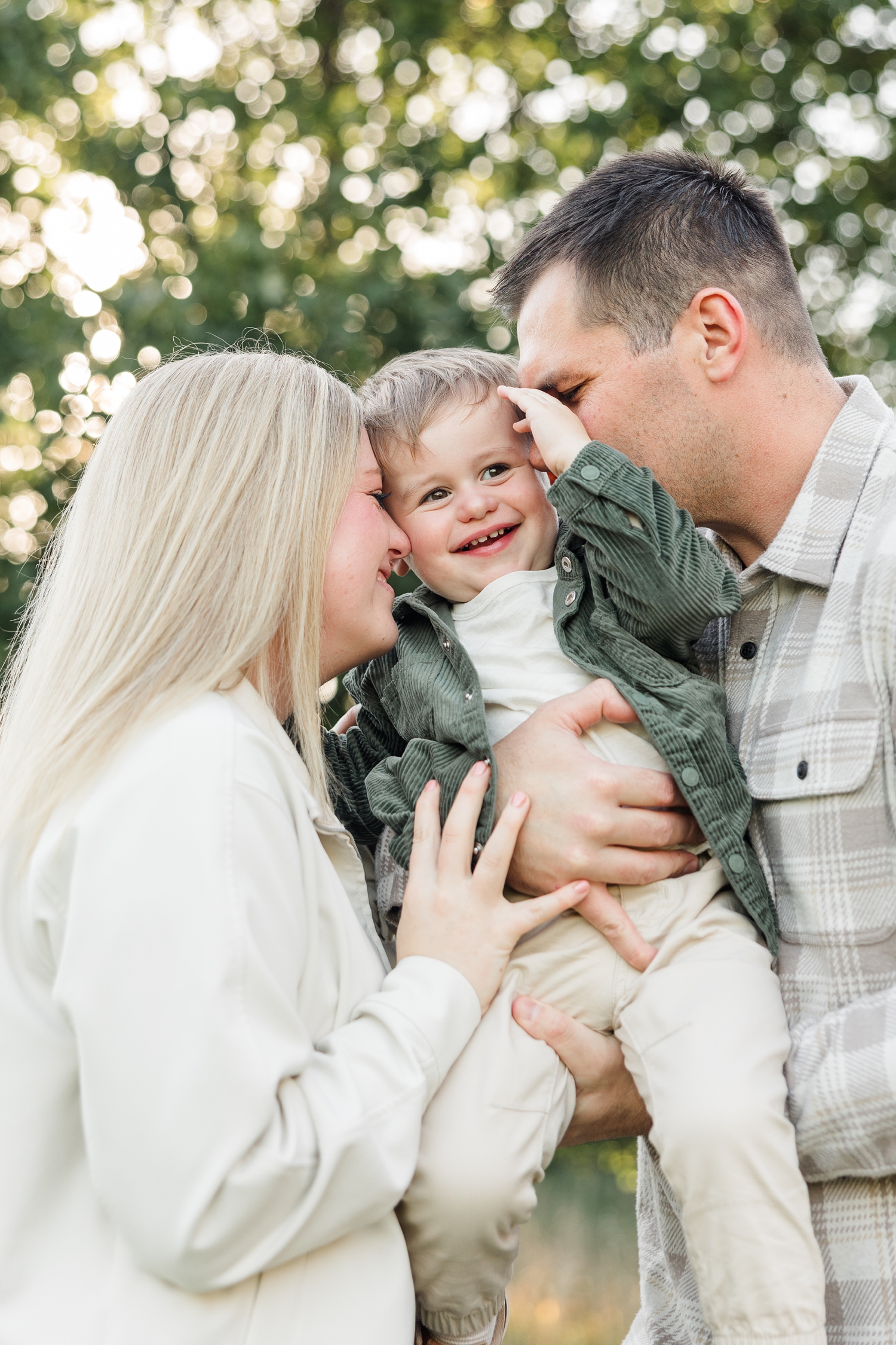 Mom and dad nuzzle their 2 year old son full of smiles with the fall leaves adorning the background | CB Studio