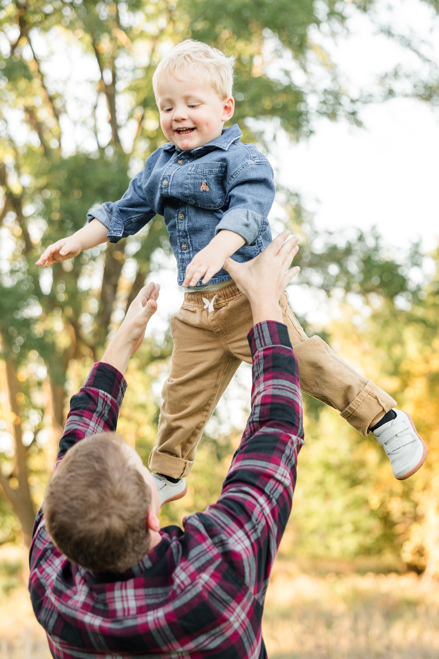 Matt throws his 2 year old son in the air as he is full of smiles and the fall leaves adorn the background | CB Studio